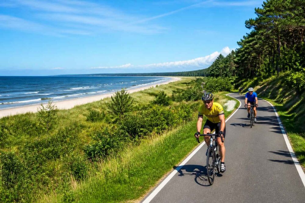 Dwóch rowerzystów jedzie ścieżką wzdłuż piaszczystej plaży i wybrzeża Bałtyku