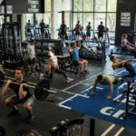 Osoby ćwiczące na wolnych ciężarach, bieżniach i sprzęcie fitness w przestronnej siłowni